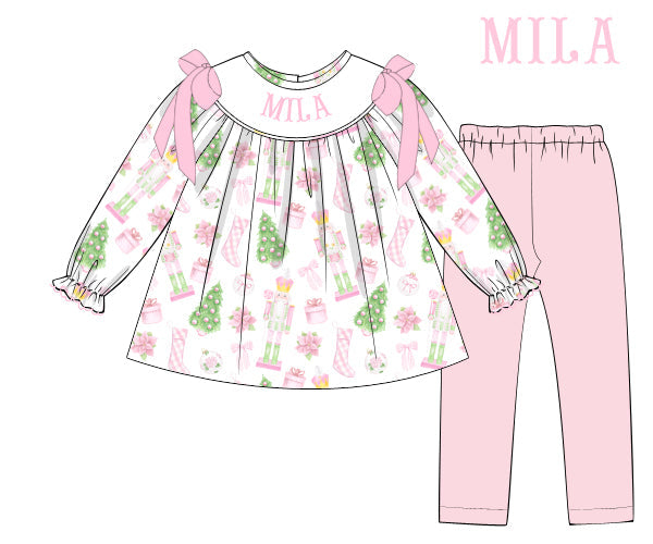 A flat technical illustration of a children's two-piece outfit set labeled 'MILA' and 'ribbon matching'. The set includes a long-sleeve top with a white base, pink bow details at the shoulders, and a festive multicolor print, paired with solid light pink pants.