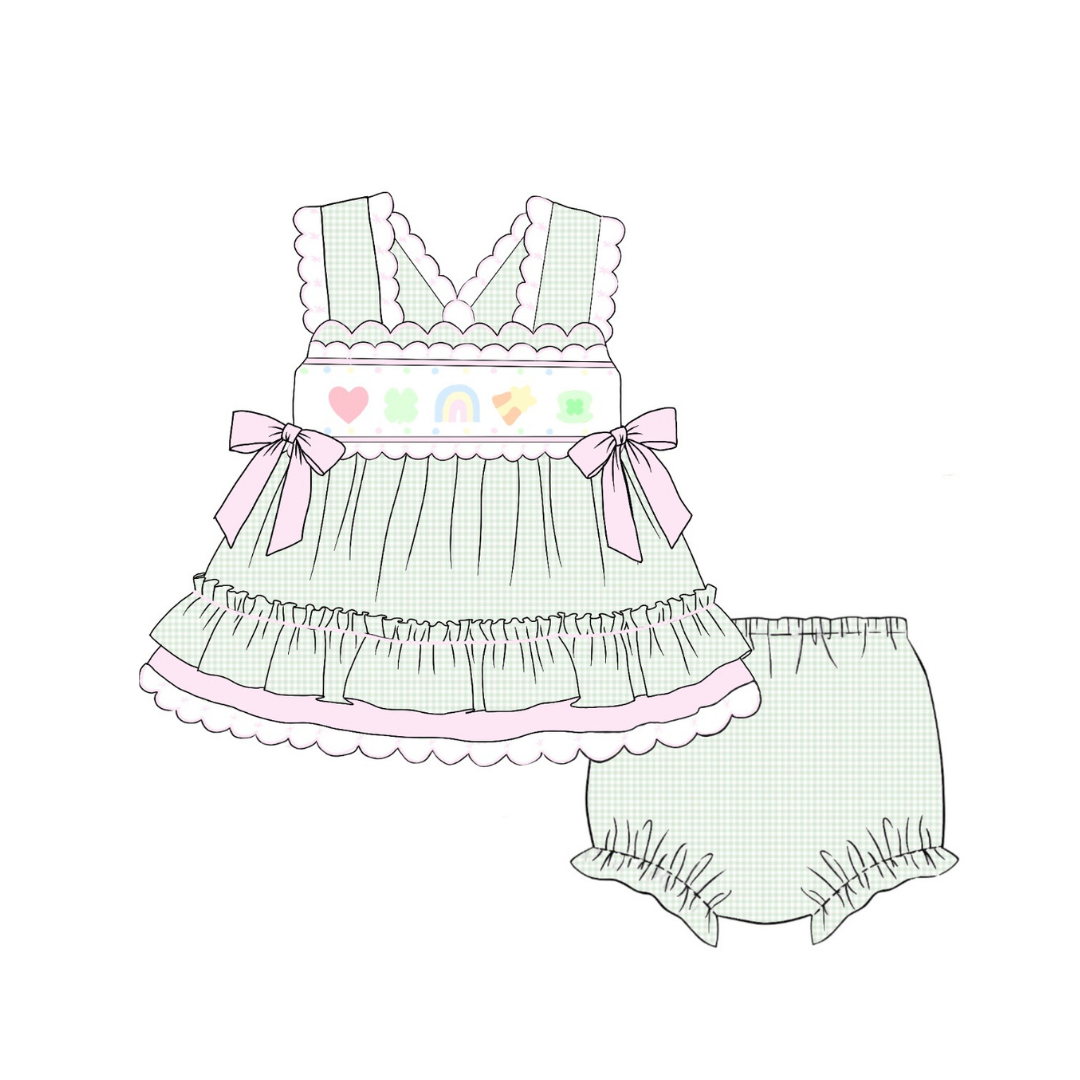 A pastel-colored baby outfit illustration featuring a ruffled sleeveless top with pink bows and a white embroidered chest panel, paired with matching ruffled bloomers, on a plain white background.