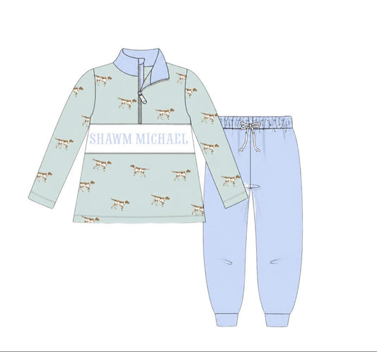 A children's two-piece pajama set shown as a flat illustration, featuring a long-sleeve quarter-zip top in pale mint green with a white chest panel and small dog prints, paired with light blue jogger pants with a drawstring waist.