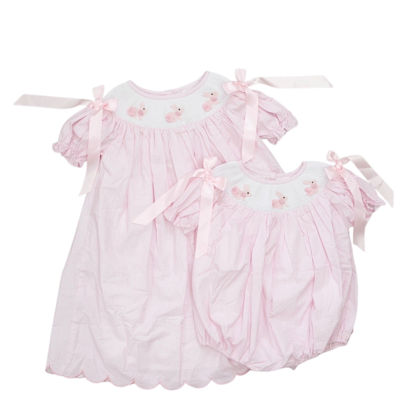 Two pink baby dresses with ruffles and bow details on a white background