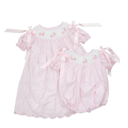 Two pink baby dresses with ruffles and bow details on a white background