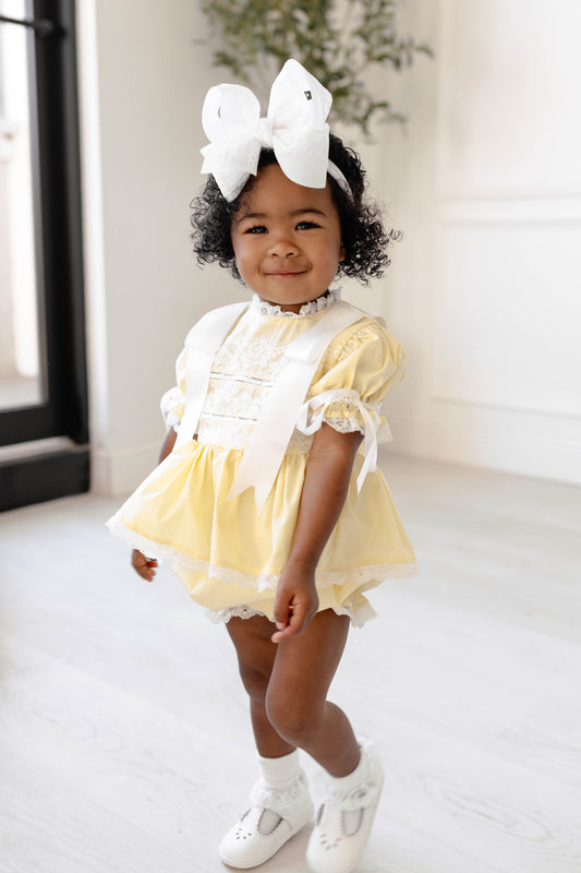 Child wearing a yellow dress with a large white bow in a bright room