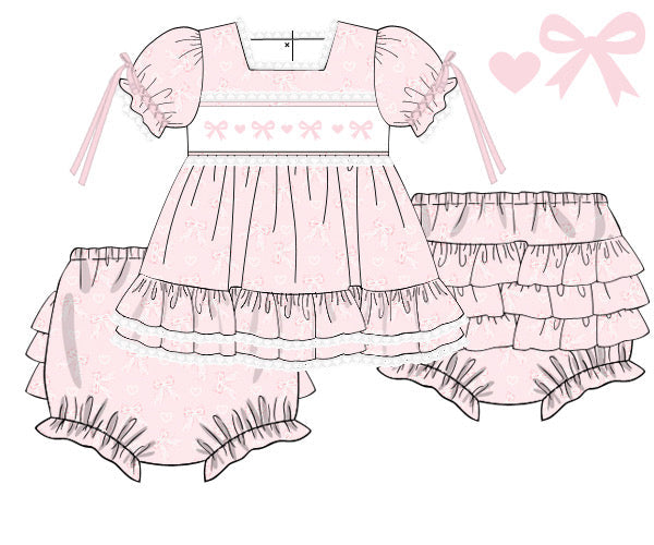 A pink and white custom woven baby dress set illustration featuring a tiered dress with puff sleeves, matching ruffled bloomers, and a ruffled diaper cover, shown on a white background with a small text label in the bottom left corner.