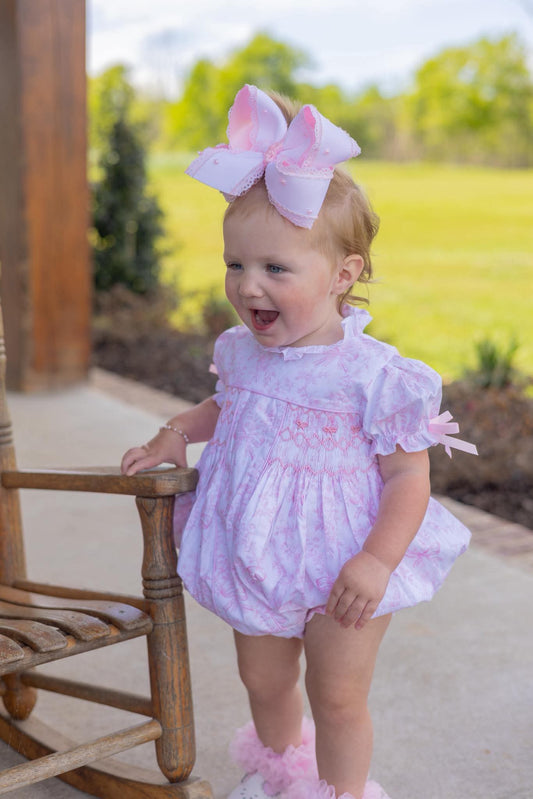 Baby girl in a pink outfit with a large bow outdoors