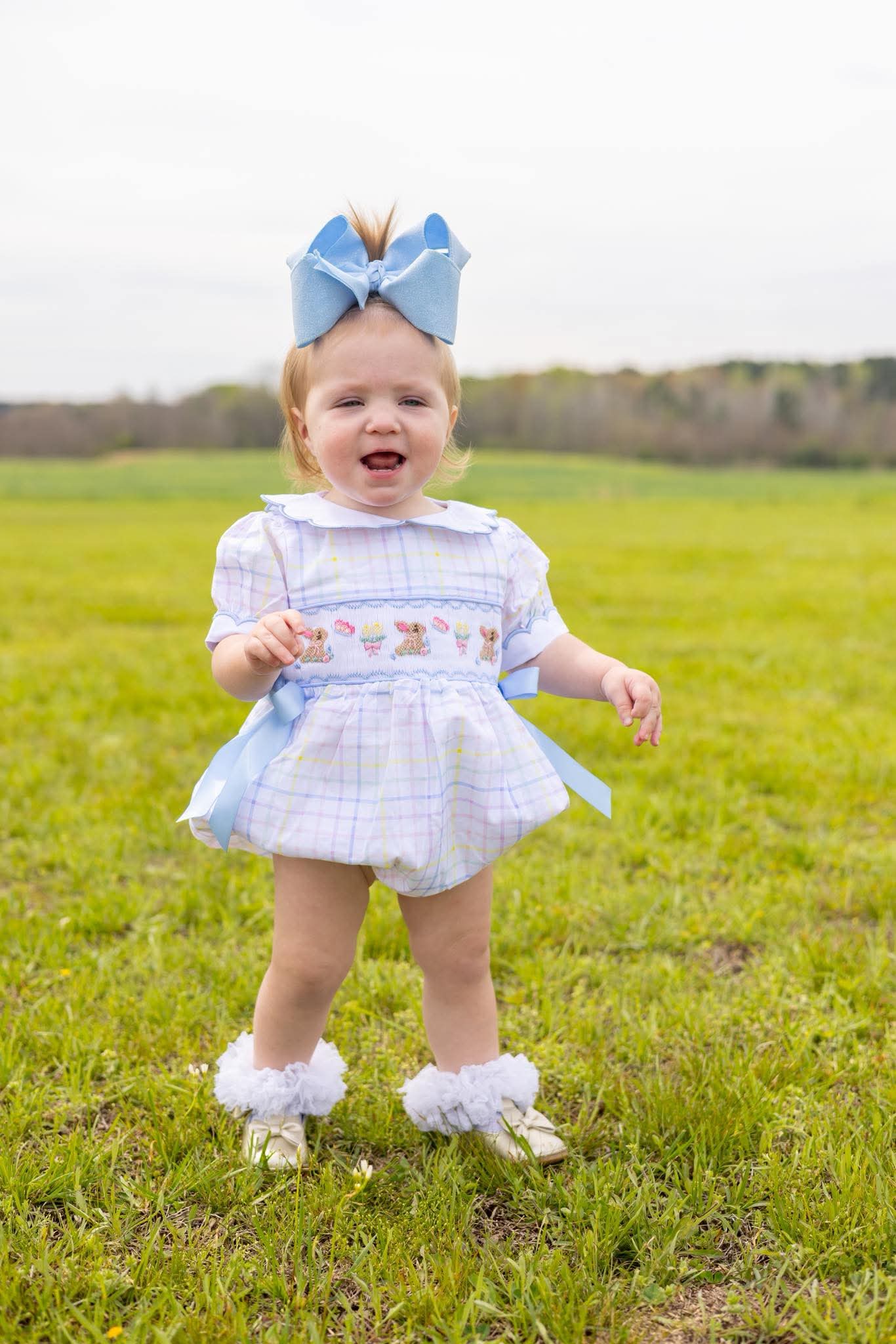 Child in a checkered dress with a blue bow standing in a grassy field