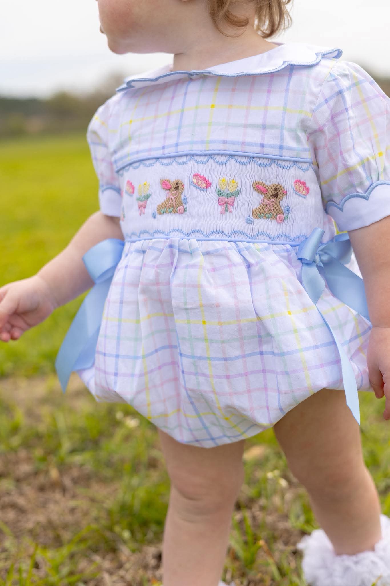 Child wearing a colorful outfit with plaid pattern and embroidered details outdoors.