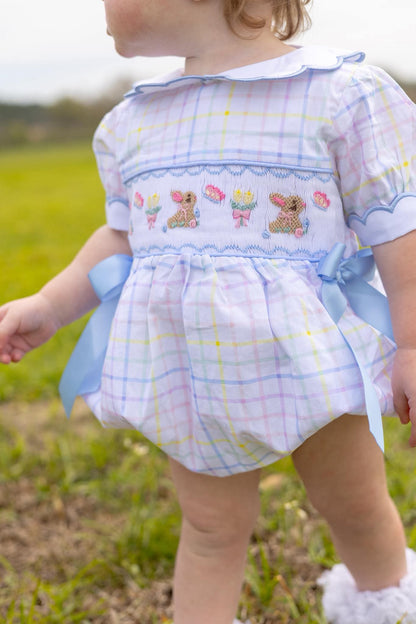 Child wearing a colorful outfit with plaid pattern and embroidered details outdoors.