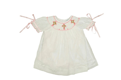 White baby dress with floral embroidery and pink ribbons on a white background