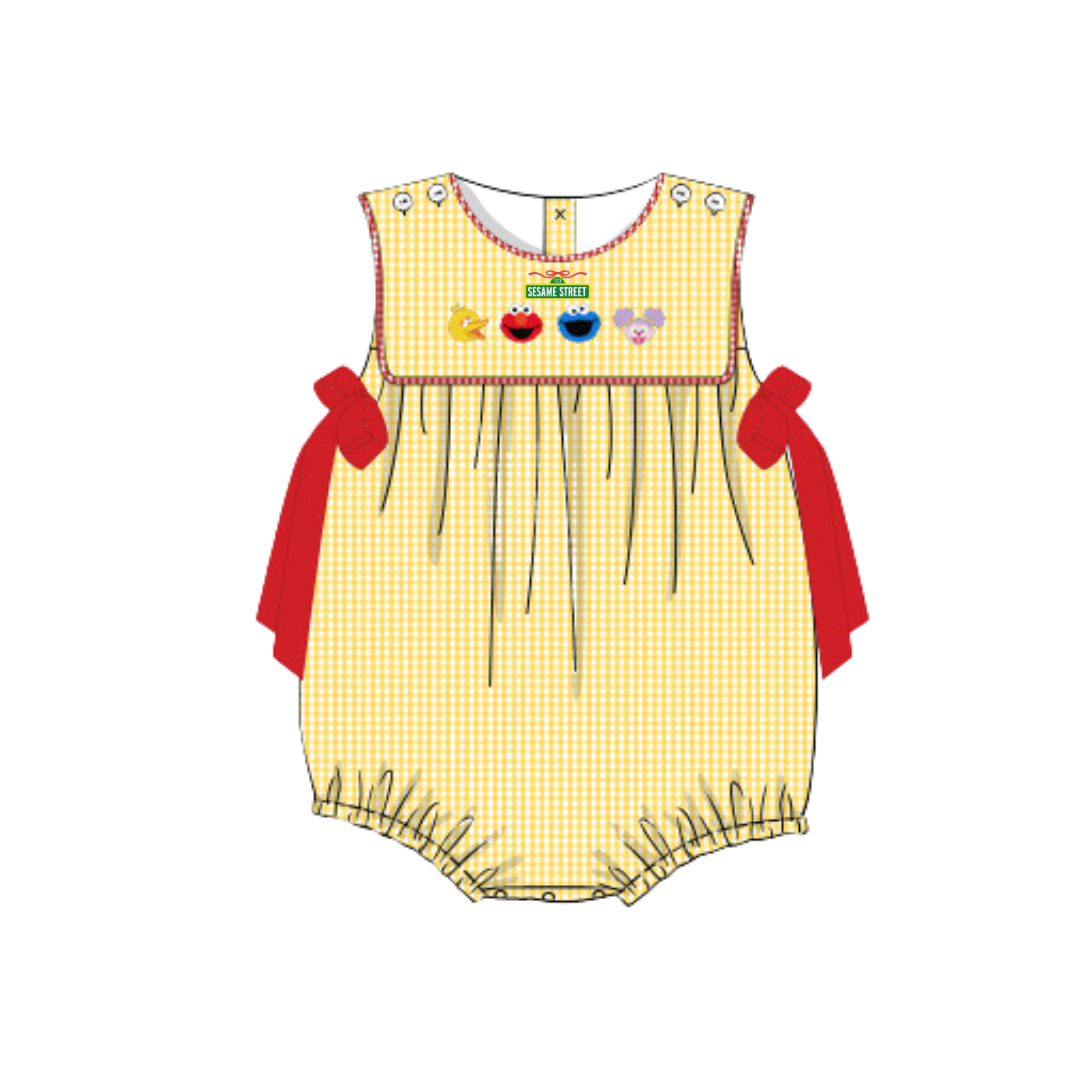 A baby romper in a pale yellow and white gingham pattern, featuring a smocked chest with colorful appliques, red side bows, and a ruffled hem.