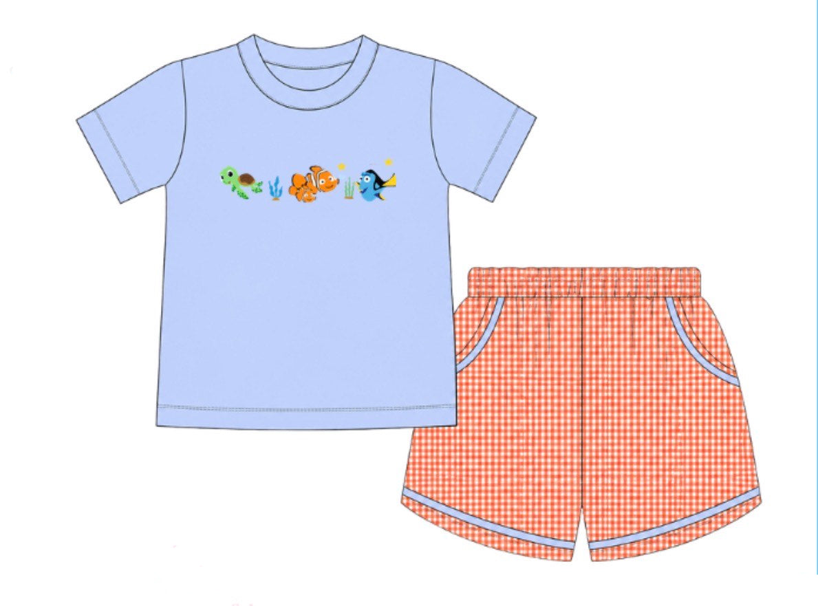 A children's two-piece pajama set shown as a flat illustration on a white background. The set includes a light blue short-sleeve top with a colorful cartoon turtle graphic across the chest and matching shorts in a red-and-white gingham pattern with light blue piping.